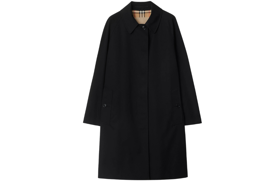 A long black trench coat with a classic collar, button closure, and side pockets. The interior lining features a beige plaid pattern. The coat is displayed against a white background.