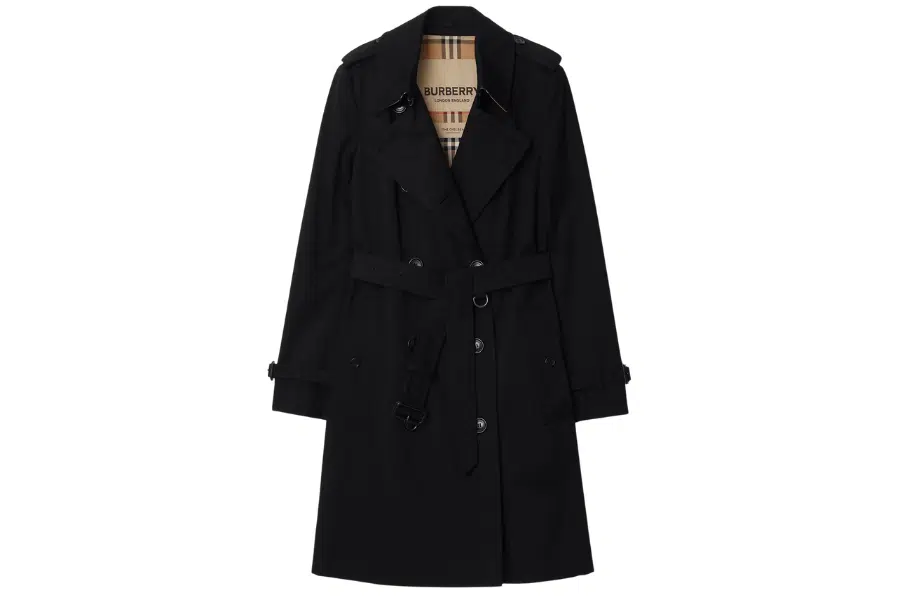 A black trench coat with a belted waist, double-breasted button front, and a tan plaid lining visible at the collar. The coat features shoulder epaulets and buttoned cuffs.