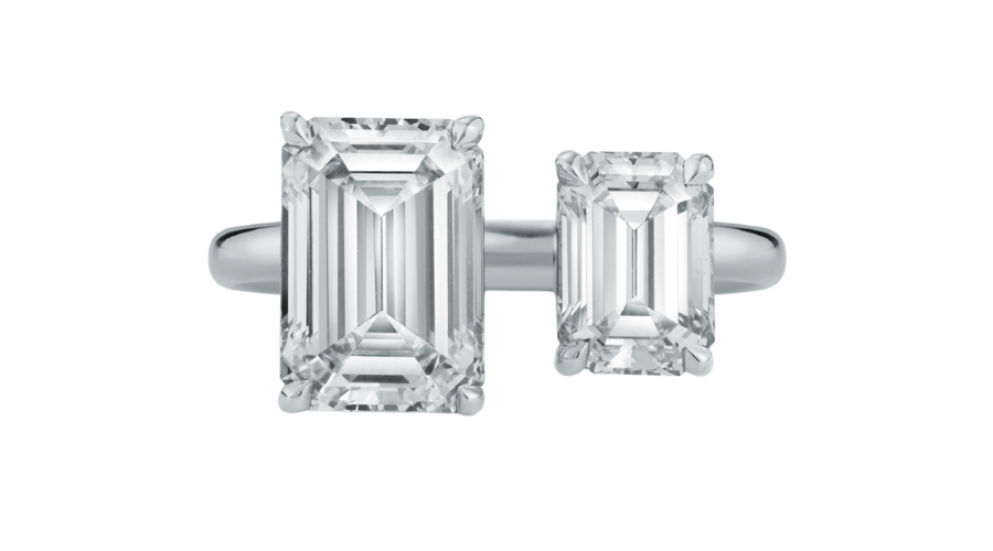 A silver ring featuring two emerald-cut clear gemstones of different sizes, set side by side on a plain band against a white background.