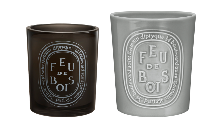 Two Diptyque Feu de Bois candles: one in a dark translucent glass holder and one in a light gray opaque holder, both featuring the brands signature oval label design on the front.