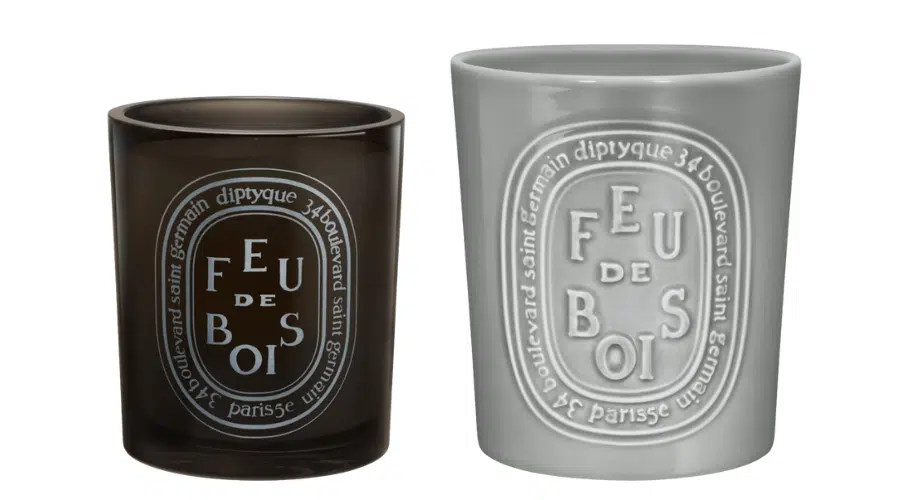 Two Diptyque Feu de Bois candles: one in a dark translucent glass holder and one in a light gray opaque holder, both featuring the brands signature oval label design on the front.