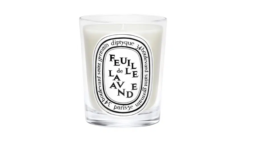 A clear glass candle labeled Feuille de Lavande by Diptyque, featuring a white wax interior and an oval black-and-white logo with decorative text around it.