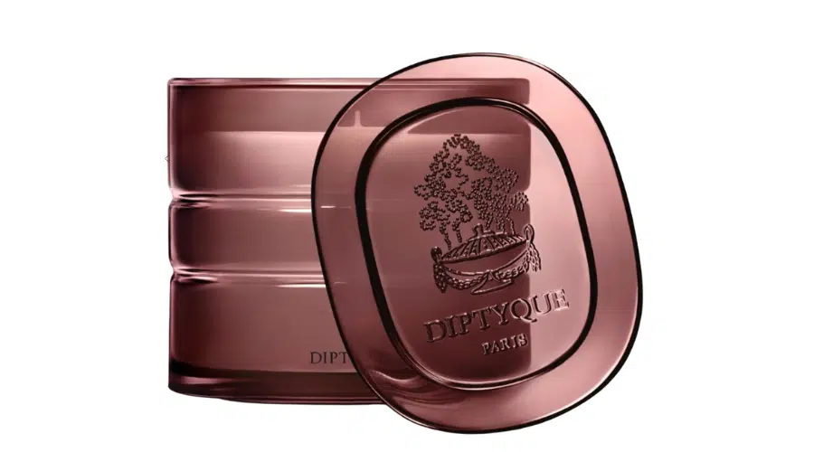 A tinted glass candle jar with a matching lid, both embossed with the Diptyque Paris logo featuring a tree and boat design. The jar and lid are a translucent mauve color on a white background.