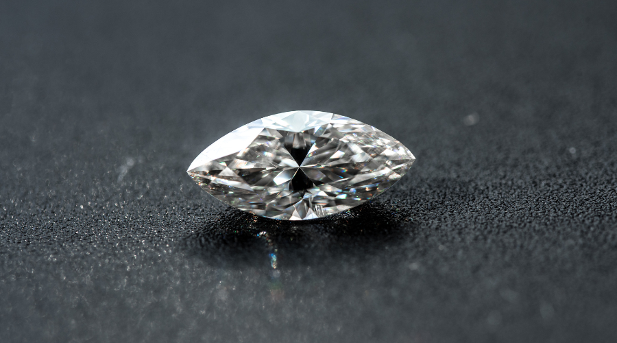 A marquise-cut diamond rests on a dark, textured surface, reflecting light and displaying its sharp facets and brilliant sparkle.