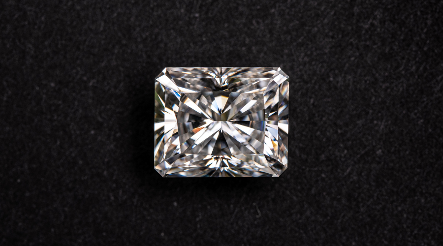 A radiant-cut diamond with sharp corners and intricate facets sparkles against a textured black background.