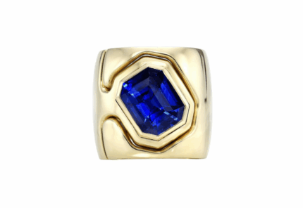 A wide gold ring featuring a large, rectangular blue gemstone set in the center, with abstract gold detailing surrounding the stone.