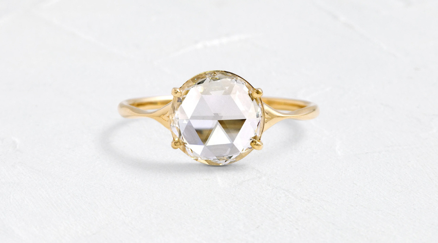 A gold ring with a large, oval, clear gemstone set in a four-prong setting, displayed on a light, textured surface.