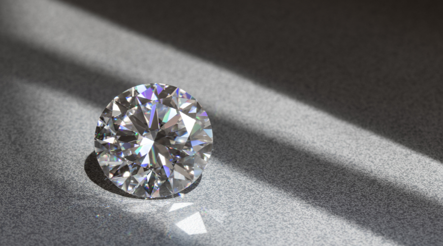 A round, faceted diamond sits on a gray surface, illuminated by diagonal beams of light, casting reflections and rainbow-like sparkles.