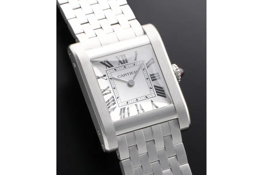 A silver Cartier wristwatch with a rectangular face, Roman numerals, and a linked metal band is displayed against a black background. The watch hands point to 10:08.