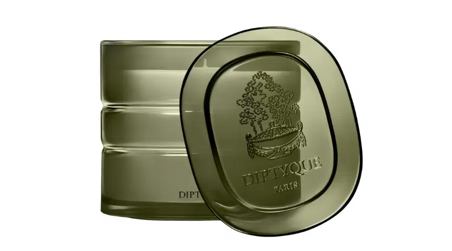 An olive green Diptyque Paris glass container with a matching oval lid, both featuring an embossed design of a tree and a boat, and the word DIPTYQUE PARIS on the front.