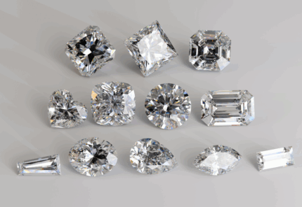 A collection of twelve diamonds, each with a different cut, including round, heart, emerald, oval, pear, cushion, marquise, radiant, and princess shapes, displayed on a light gray surface.