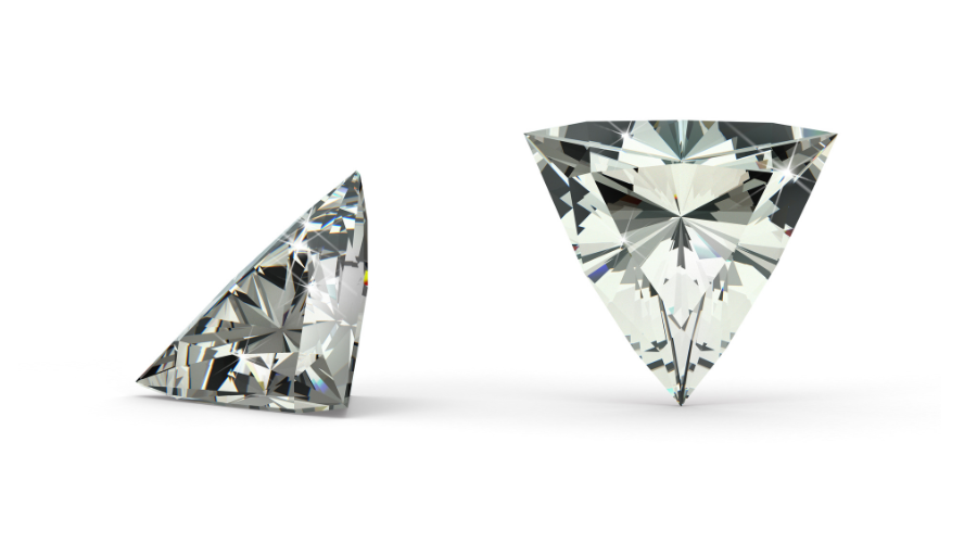 Two triangular-shaped, clear gemstones are displayed on a white background; one is standing upright, and the other is lying on its side, showcasing their facets and brilliance.