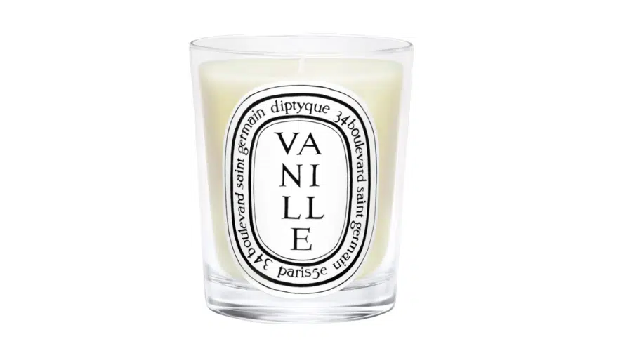 A white candle in a clear glass holder with a black and white oval Diptyque label reading Vanille and 34 boulevard saint germain paris.