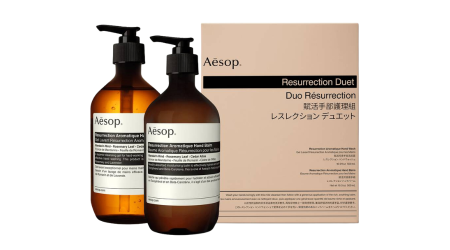 Two amber pump bottles labeled Aesop Resurrection Aromatique Hand Wash and Hand Balm stand in front of a beige Aesop box labeled Resurrection Duet in English and Japanese.