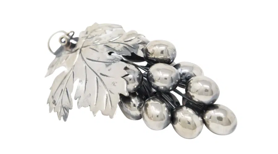 A silver ornament shaped like a cluster of grapes with a detailed leaf attached, all made from shiny metal, shown on a white background.