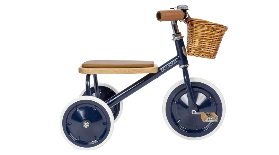 A navy blue tricycle with white tires, a tan seat, brown handlebars, and a wicker basket attached to the front.