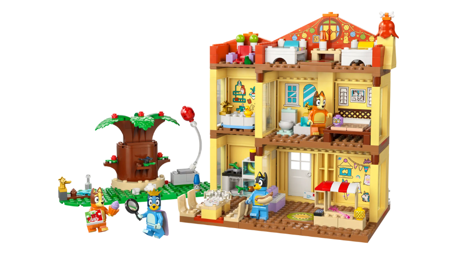 A colorful toy playset depicting a two-story house with detailed rooms, accessories, and four animated dog character figures. A tree and small outdoor scene are included on the left side.