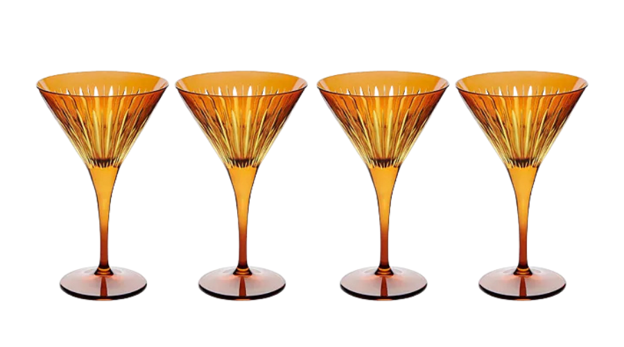 Four amber-colored martini glasses with fluted designs are arranged in a row against a white background.