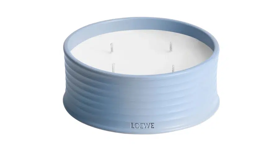 A large, round, pale blue ribbed candle holder with four wicks and LOEWE embossed on the side. The candle is filled with white wax.