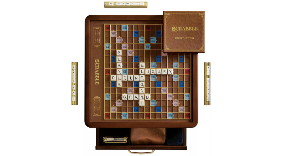 A Scrabble Luxury Edition board game set, featuring a brown rotating board with tiles forming words like PLAYER, LUXURY, ELEGANT, GRAND, and REFINE. The box and trays for letter tiles are also visible.