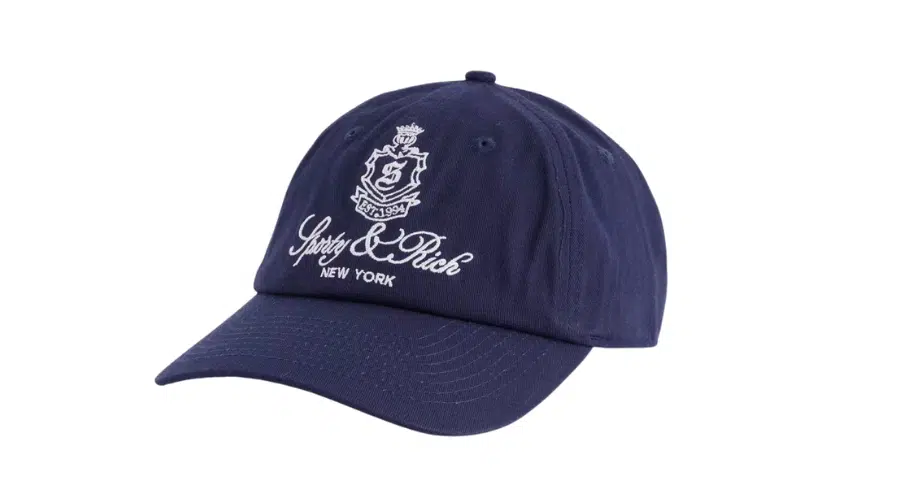 A navy blue baseball cap with a curved brim, featuring a white embroidered crest and the words Sporty & Rich NEW YORK on the front. The background is plain white.