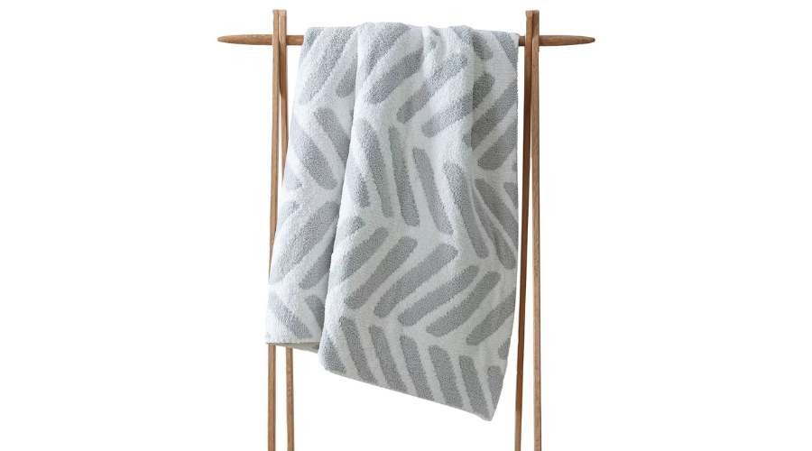 A soft, light gray and white patterned towel is draped over a simple wooden towel rack against a plain white background.