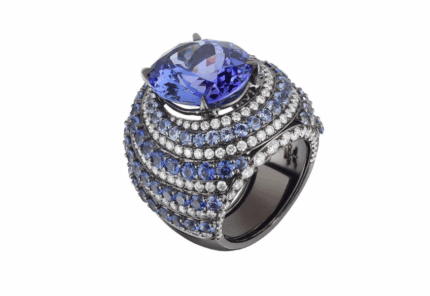 A luxurious ring featuring a large, cushion-cut blue gemstone at the center, surrounded by rows of smaller blue and clear stones set in a bold, dark metal band.