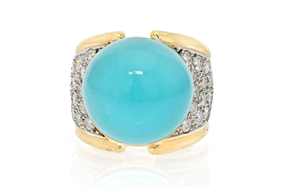 A gold ring featuring a large, round turquoise stone at the center, flanked by sections encrusted with small, sparkling white diamonds on each side.