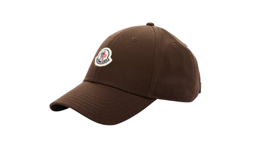 A brown baseball cap with visible stitching and a curved brim, featuring a small embroidered patch logo on the front panel. The background is plain white.