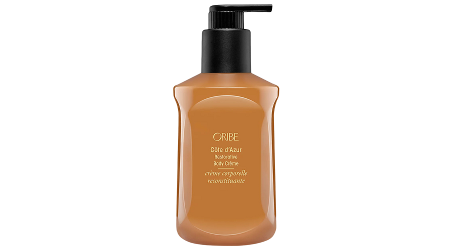 A brown bottle of Oribe Côte d’Azur Restorative Body Crème with a black pump dispenser and gold text on the front, shown against a white background.