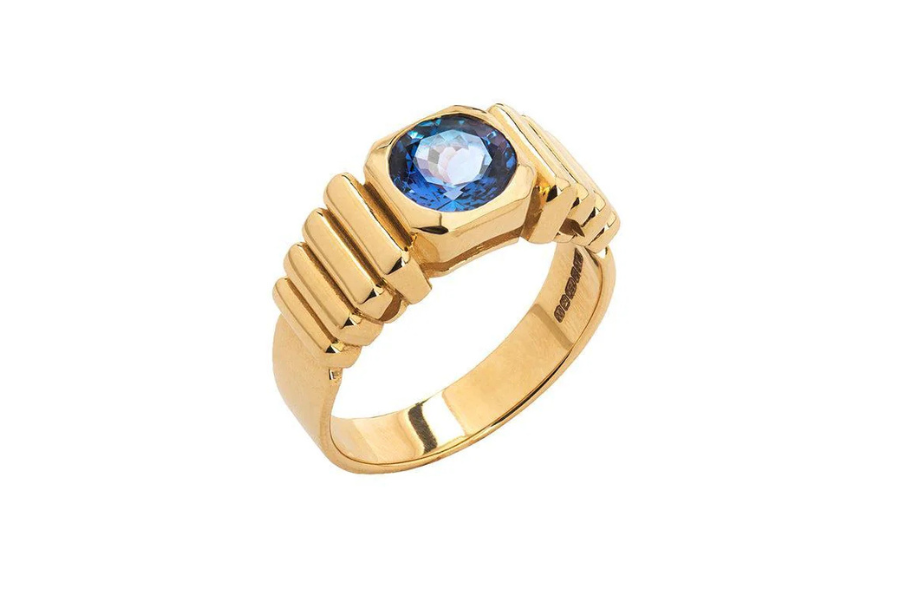 A gold ring with a chunky, ridged band featuring a round blue gemstone set in the center.