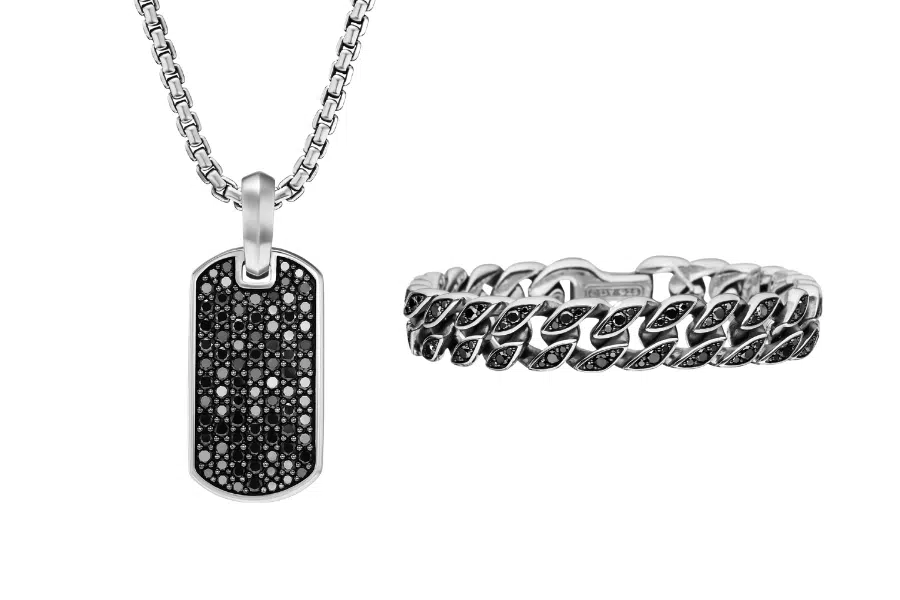 A silver dog tag necklace with a black gemstone-encrusted pendant beside a matching silver chain-link ring, both featuring black gemstone accents, displayed on a white background.