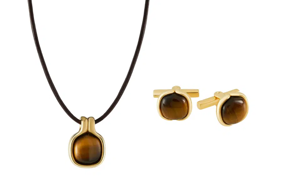 A matching jewelry set with a tiger’s eye pendant on a black cord necklace and a pair of gold-framed tiger’s eye cufflinks on a white background.
