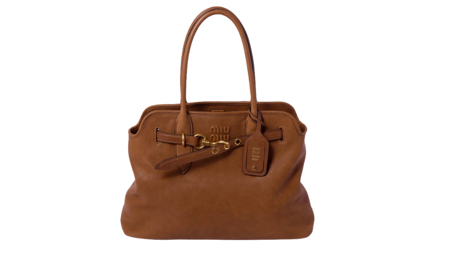 A large brown leather handbag with two handles, a gold buckle, a hanging leather tag, and the brand Miu Miu embossed on the front. The bag is set against a white background.