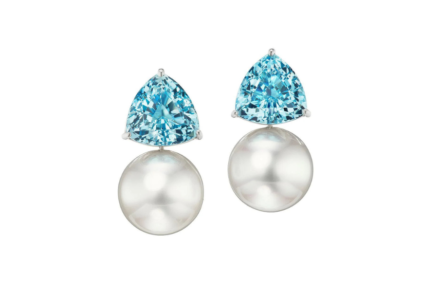 A pair of earrings featuring a triangular blue gemstone on top and a round white pearl below, set in a minimalist metal setting.