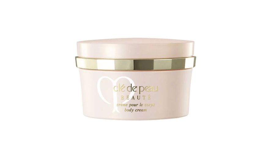 A beige jar of Clé de Peau Beauté body cream with a gold-accented lid and gold lettering on the front, set against a white background.