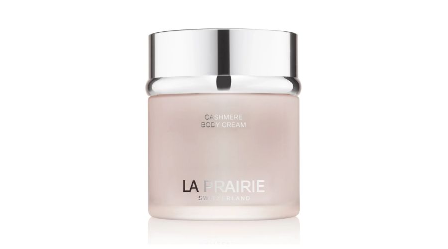 A frosted glass jar with a shiny silver lid labeled Cashmere Body Cream and La Prairie Switzerland in sleek white and silver text.