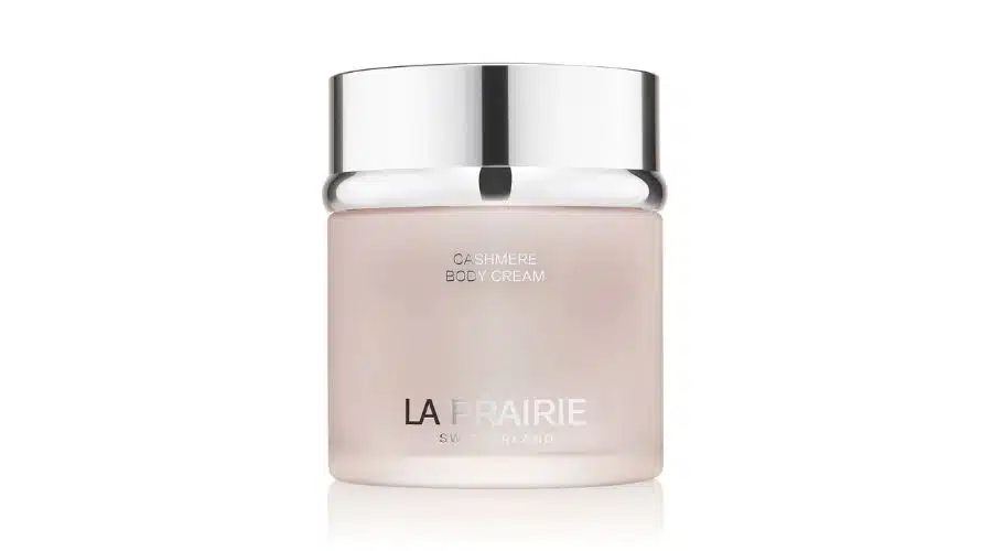 A frosted glass jar with a shiny silver lid labeled Cashmere Body Cream and La Prairie Switzerland in sleek white and silver text.