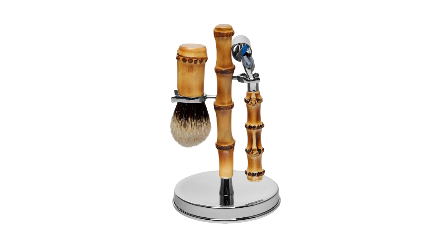 A shaving set with bamboo handles, including a brush and a razor, displayed on a round chrome stand against a white background.