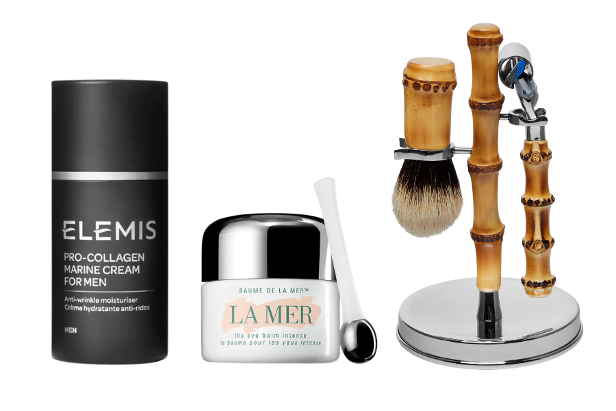 Three mens grooming products: a black bottle of Elemis Pro-Collagen Marine Cream, a white jar of La Mer The Eye Balm Intense with a small applicator, and a shaving brush and razor set with bamboo handles on a stand.