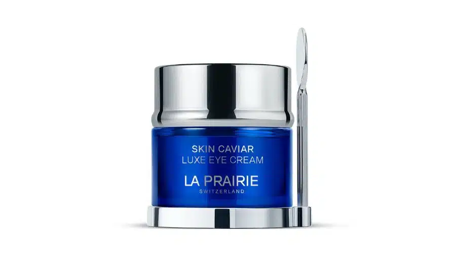 A blue and silver jar of La Prairie Skin Caviar Luxe Eye Cream with a small silver spatula resting on its side, set against a white background.