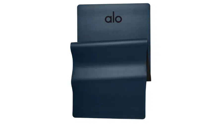 A dark blue Alo yoga mat is partially unrolled, showing the brand logo alo at the top center of the mat against a plain white background.