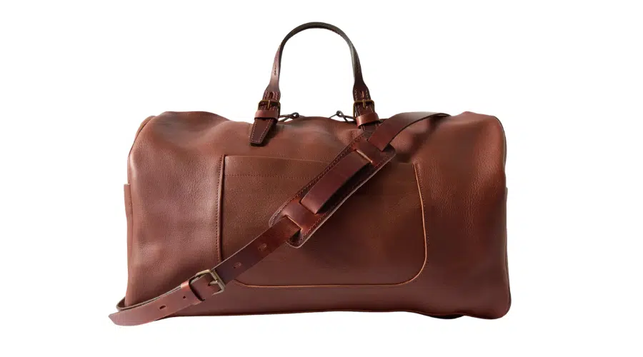 A large brown leather duffel bag with a top handle, front pocket, and an adjustable shoulder strap, shown against a white background.