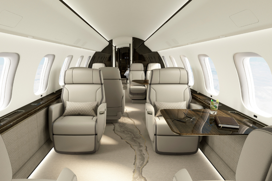 Interior of a modern private jet featuring spacious beige leather seats, large windows, a fold-out table with a drink and a notebook, and elegant lighting, creating a luxurious and comfortable atmosphere.