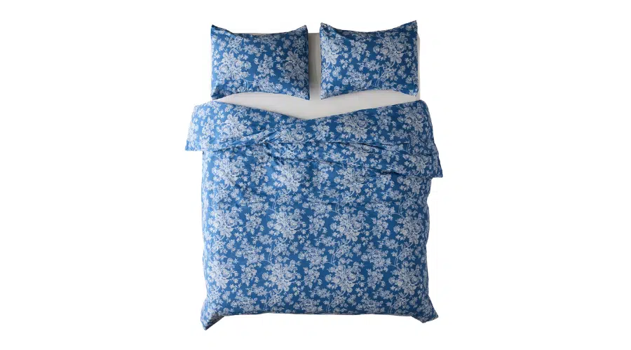 Top view of a bed with blue bedding and two pillows, all featuring a white floral pattern on the fabric, against a white background.